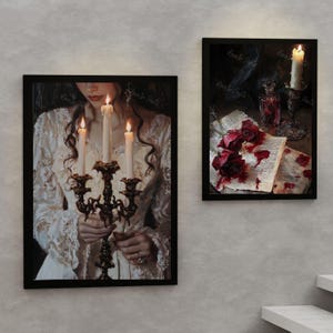May include: Two framed paintings, one depicting a woman in a white dress holding a candelabra with lit candles, the other showing a book with red roses and bloodstains.