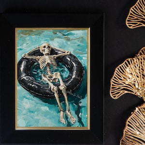 May include: A watercolor painting of a skeleton floating on an inner tube in a turquoise pool. The skeleton is wearing a relaxed pose with arms outstretched and legs crossed. The painting is framed in black.