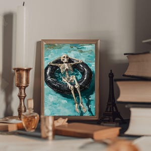 May include: A framed painting of a skeleton floating in a pool on an inner tube. The skeleton is wearing a relaxed pose with its arms outstretched. The water is a turquoise blue color and the inner tube is black.