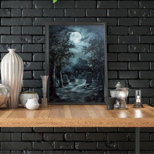 May include: A framed painting of a graveyard at night with a full moon in the sky. The painting is in a black frame and is hanging on a black brick wall. There are various decorative items on a wooden table in front of the painting.