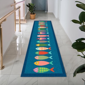 May include: A blue rectangular runner rug featuring a repeating design of vibrant fish. The fish are decorated with diverse patterns and colours, such as stripes, spots, and diamond shapes. The rug is laid in a hallway with white walls and a tiled floor.