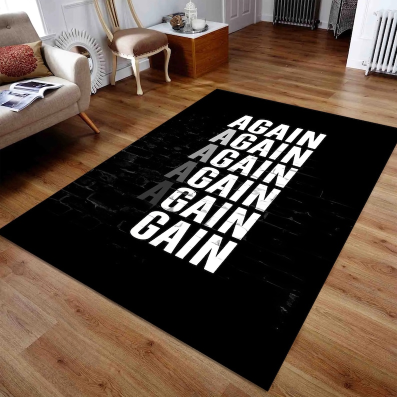 K&ouml;nnte beinhalten: Schwarzer rechteckiger Teppich mit dem Wort "AGAIN" in einem vertikalen Muster. Das Wort ist wei&szlig;, mit einer grauen Instanz. Der Teppich hat eine ziegelartige Textur auf der linken Seite.