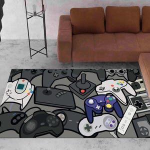 May include: A rectangular area rug featuring a repeating pattern of various video game controllers in shades of gray, black, white, and purple. The design includes illustrations of classic handheld and console gamepads, joysticks, and remote controls.