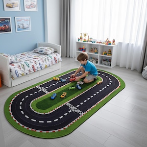 May include: An oval-shaped area rug featuring a black racetrack design with white lane markings, red and white chequered borders, and green grass-like sections. The rug includes printed start and finish lines on the track surface.