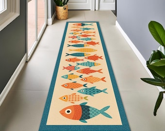May include: A long rectangular runner rug featuring a cream-colored center with a repeating pattern of stylized fish in shades of orange, red, yellow, and teal. The rug is framed by a solid teal border with a subtle textured appearance.