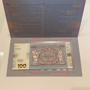 Op de afbeelding: Een herdenkingsbiljet van 100 Oekraïense hryvnia, ter viering van de 100e verjaardag van de Oekraïense Revolutie van 1917-1921. De afbeelding toont een vrouw in traditionele klederdracht en een man met een hamer. De tekst "100" is prominent aanwezig.
