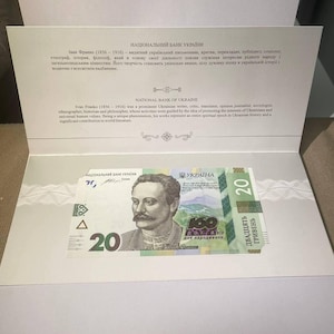 May include: A twenty Ukrainian Hryvnia banknote featuring a portrait of Ivan Franko, displayed within a white presentation folder. The banknote is green and blue, with text in Ukrainian and English.
