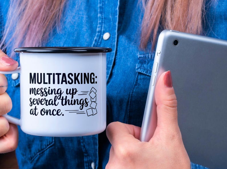 May include: White enamel mug with a black rim and handle. The mug has a black graphic that says "MULTITASKING: messing up several things at once." The graphic includes a stack of squares that are falling over.