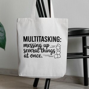 May include: White canvas tote bag with black text that reads "MULTITASKING: messing up several things at once." The text is stylized with a series of black lines and squares.