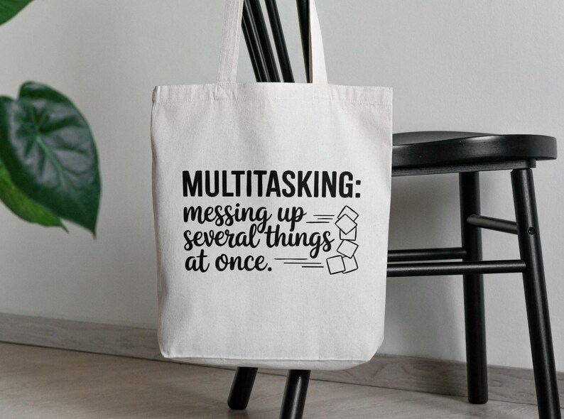 May include: White canvas tote bag with black text that reads "MULTITASKING: messing up several things at once." The text is stylized with a series of black lines and squares.