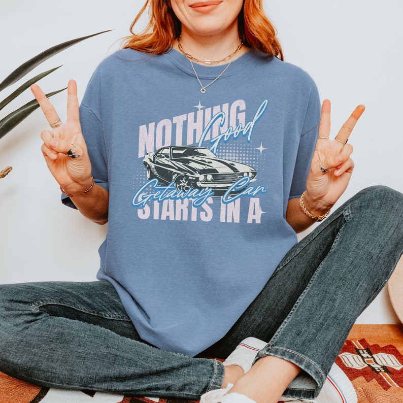May include: A blue t-shirt with a graphic of a black muscle car and the text "Nothing Good Getaway Can Start In A".