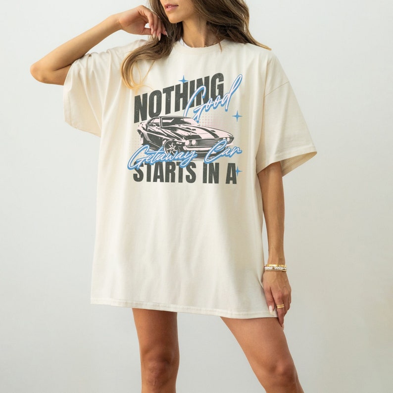 May include: A cream colored oversized t-shirt with a graphic print of a black muscle car and the text "Nothing good starts in a getaway car".