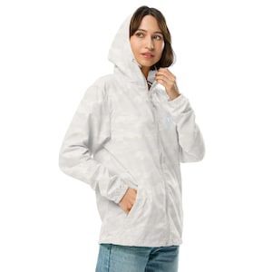 May include: White camouflage hooded jacket with a full zipper closure and two front pockets. The jacket features a small, light blue embroidered design on the chest. The model is wearing the jacket.