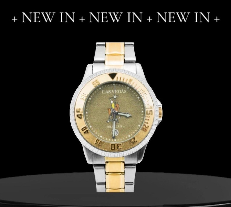 May include: A two-tone gold and silver wristwatch with a black face and a gold-colored Las Vegas Polo Club logo. The watch has a black bezel with white numbers and a date window at the 3 o'clock position.