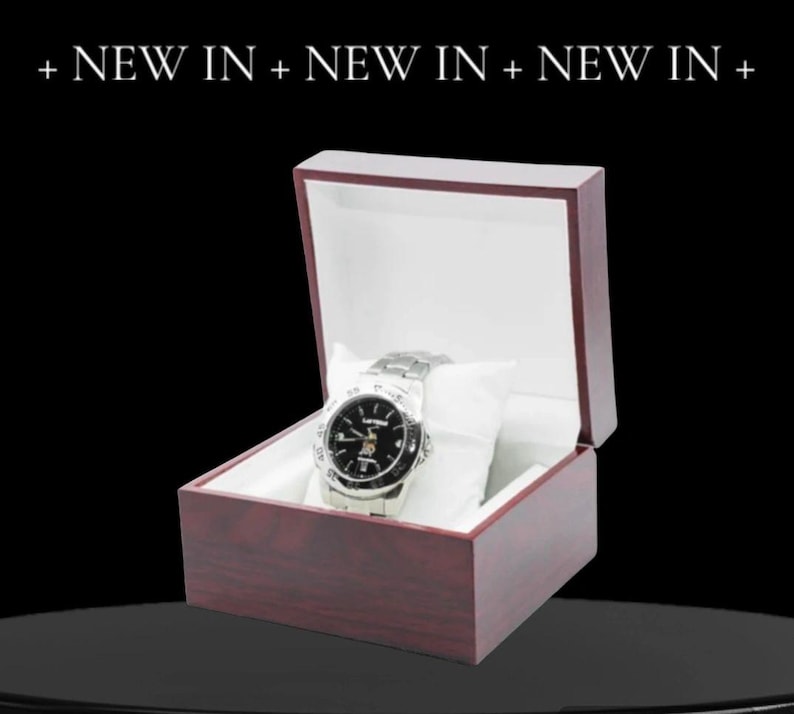 May include: A silver wristwatch with a black face and silver hands in a dark red wooden box with a white interior.