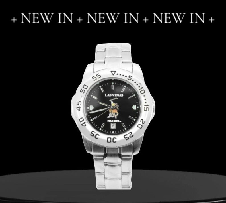 May include: A silver wristwatch with a black face and a silver band. The watch face has a white border with black numbers and a white triangle at the top. The watch face also has the words "LAS VEGAS" and "POLO CLUB" printed on it.