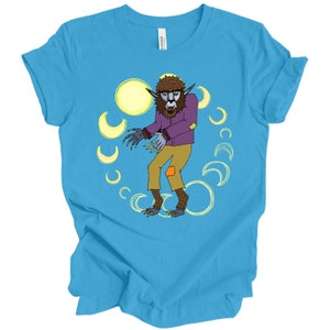 May include: A turquoise blue t-shirt with a cartoon werewolf wearing a purple shirt and brown pants. The werewolf is surrounded by yellow crescent moons.