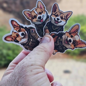 May include: Three cartoon stickers of corgis wearing military uniforms. The corgis are brown and white with floppy ears. The stickers are on a white background.