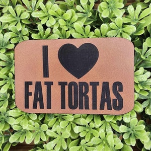 May include: Brown leather patch with the text "I heart Fat Tortas" in black lettering. The heart is a black silhouette.