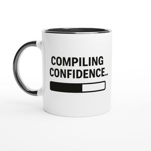 May include: White ceramic mug with a black interior and handle. The mug displays the text "COMPILING CONFIDENCE.." in black, and a black and white progress bar graphic. The mug is suitable for hot drinks.