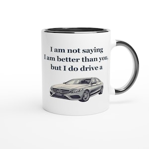Könnte beinhalten: Weißer Keramikbecher mit schwarzem Rand und Henkel. Der Becher zeigt den Text "I am not saying I am better than you, but I do drive a" und eine Abbildung eines silbernen Autos. Das Auto hat den Namen "STEVE".