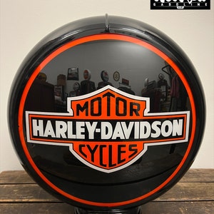 May include: A black Harley-Davidson Cycles globe with an orange and white logo. The globe has a glossy finish and an orange border. The text "MOTOR HARLEY-DAVIDSON CYCLES" is prominently displayed on the front. The globe is mounted on a black base.