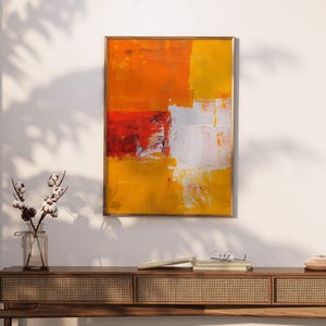 Può includere: Dipinto astratto in una cornice dorata con pennellate di colore giallo, arancione, rosso e bianco. Il dipinto è appeso a una parete bianca sopra un tavolo consolle in legno.