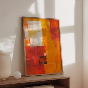 Può includere: Dipinto astratto in una cornice di legno con uno schema di colori rosso, arancione e giallo. Il dipinto è appeso a una parete sopra uno scaffale di legno.