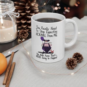 May include: White ceramic mug with a black and purple cartoon clown holding a balloon. The mug has the text "You Really Need To Stop Expecting NORMAL From Me. We Both Know That's NEVER Going to Happen!"