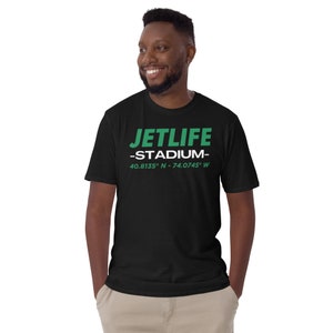 Può includere: Maglietta nera con testo bianco che dice "JETLIFE -STADIUM- 40.8135° N - 74.0745° W" in verde.