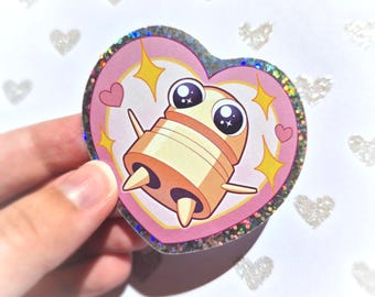 Könnte beinhalten: Ein herzförmiger Aufkleber mit einer Cartoonfigur mit großen Augen und einem zylindrischen Körper. Der Aufkleber hat einen rosa Hintergrund mit gelben Sternen und kleinen Herzen. Der Rand ist irisierend.