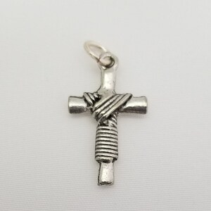May include: A silver cross pendant with a rope-like design on the front. The cross is on a white background.