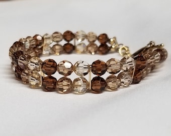 May include: A double-strand bracelet made of faceted glass beads in shades of brown and clear. The bracelet has a gold-toned clasp.