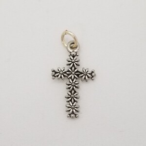May include: A silver charm in the shape of a cross, with a floral design. The cross is made up of small, daisy-like flowers.