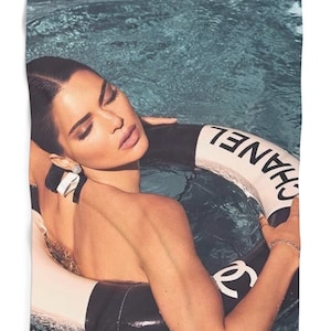 May include: A woman in a swimming pool wearing a black swimsuit and a white and black Chanel life preserver.