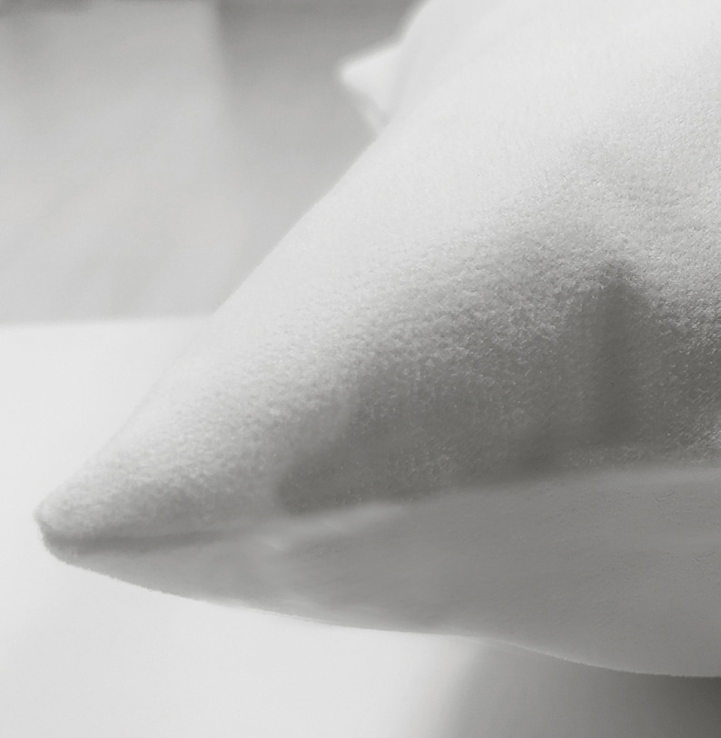 May include: Close-up of a white pillow with a textured, plush surface. The pillow is a solid white colour and has a soft, inviting appearance. The image highlights the pillow's corner, emphasising its shape and texture.