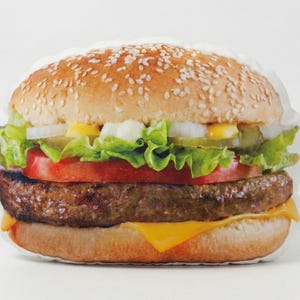 May include: A soft, cushion-like hamburger. The top bun is covered in sesame seeds, and the burger includes lettuce, tomato, onion, pickles, a beef patty, and melted cheese. It's designed to look like a classic cheeseburger.