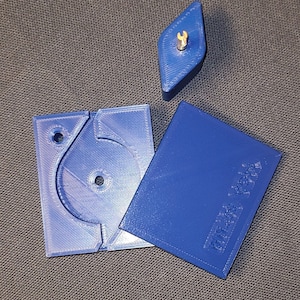 May include: A blue plastic puzzle with three pieces. The puzzle has a circular cutout and a small, diamond-shaped piece with a gold keyhole. The larger piece has the text "Puzzle Toys" printed on it.