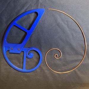 Könnte beinhalten: Ein blaues Kunststoff-Spiralwerkzeug mit dem Text "Fern Hollow Nature" und eine Kupferdrahtspirale auf dunklem Hintergrund. Das Werkzeug wird verwendet, um eine Spiralform zu erzeugen.