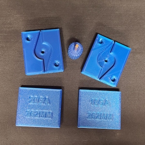 Può includere: Un insieme di componenti blu stampati in 3D. Il set include due pezzi rettangolari abbinati con un design curvo, due pezzi quadrati più piccoli con testo e un piccolo pezzo a forma di ingranaggio. Il testo sui quadrati recita "20GA 262MM" e "18GA 262MM".