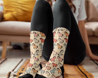 May include: A pair of socks with a colorful cartoon horse pattern. The socks are cream colored with a variety of colored horses, including pink, orange, brown, and gray. The socks are worn by a person with their legs crossed.