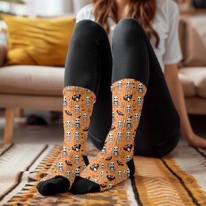 May include: A pair of orange and black socks with a Halloween theme. The socks feature a repeating pattern of skeletons, bats, pumpkins, and candy corn.