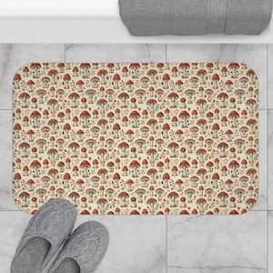 Puede incluir: Una alfombra de baño de color crema con un patrón repetido de setas rojas y blancas. Las setas están dibujadas en un estilo vintage sobre un fondo marrón claro.