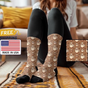 Könnte beinhalten: Ein Paar braune und beige Socken mit einem Muster aus Comic-Kaffeetassen. Die Socken liegen auf einem braunen und beigen Teppich. Die Socken sind in den USA hergestellt.