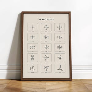 May include: A framed print titled "Sacred Circuits" featuring a beige background with a grid of black geometric symbols. The symbols are enclosed in small squares, and the print is in a dark brown wooden frame. The print is leaning against a white wall.