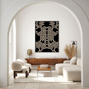 May include: A living room interior with a modern, abstract black and beige wall art print hanging above a wooden console table. The room features a white couch, two white armchairs, a coffee table, and a floor lamp.