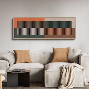 May include: Abstract geometric wall art in a wooden frame. The artwork features rectangular blocks of color in shades of orange, green, brown, and beige, with vertical lines. The artwork hangs above a light-colored sofa with brown throw pillows.