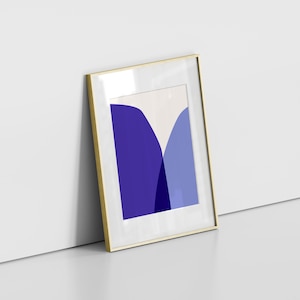 May include: A framed art print featuring an abstract design with shades of blue and a cream background. The artwork is enclosed in a gold-colored frame with a white mat. The print is leaning against a white wall.