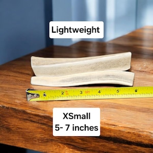 May include: Two antler dog chews, one on top of the other, are measured with a yellow tape measure. The chews are described as "Lightweight" and "XSmall 5-7 inches".