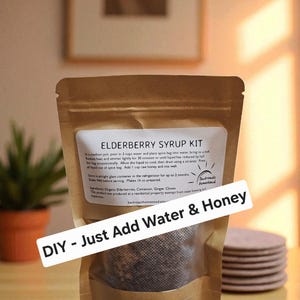May include: A brown paper pouch labeled Elderberry Syrup Kit with instructions to add water and honey. The label lists organic elderberries, cinnamon, ginger, and cloves as ingredients. A white banner across the front reads DIY - Just Add Water & Honey.